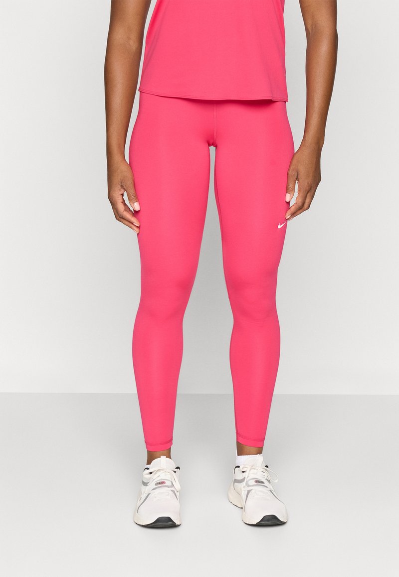 Leggings de sport roses en tissu extensible, avec une texture lisse et un petit logo blanc près de la taille, associés à des baskets blanches.