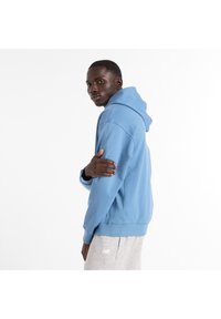 Sudadera con capucha en tela azul claro, con un ajuste holgado, puños y cinturilla acanalados, combinada con pantalones deportivos grises.