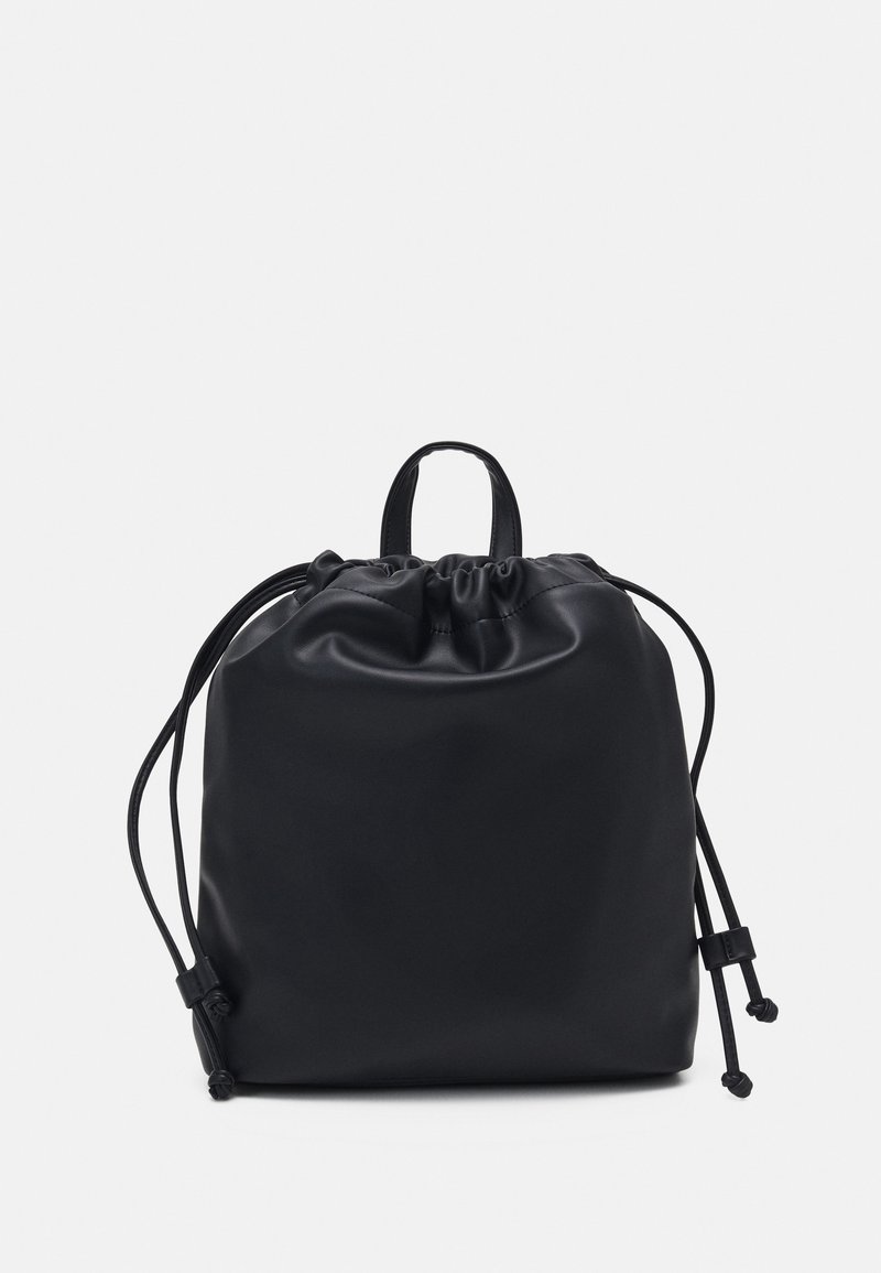 Petit sac à dos noir en cuir avec cordon de serrage, poignée supérieure et cordons latéraux réglables sur un fond blanc uni.