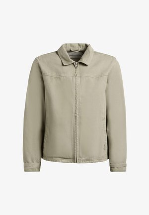 Bézs színű zipzáras dzseki gallérral, hosszú ujjakkal és oldalzsebekkel, fehér háttér előtt bemutatva.