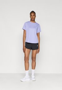 Lilla lühikeste varrukatega sportpingutus, millel on ümmargune kaelus, koos mustade lühikestega. Mudel kannab valgeid jooksujalatseid ja kummisukke. Lihtne disain ja sobivus.