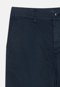 Pantaloni blu navy in tessuto liscio con vestibilità slim, dotati di chiusura con bottoni e tasche laterali, mostrati dalla vita in giù.