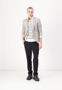 Blazer gris clair sur un pull rayé crème et marine, associé à un pantalon foncé et des baskets noires. Textures lisses, coupe ajustée.