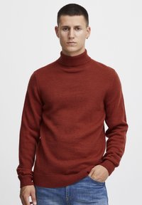 Pulover turtleneck roșu ruginit fabricat dintr-o țesătură moale. Are manșete și tiv cu nervuri, cu o siluetă ajustată. Purtați-l cu blugi albaștri.