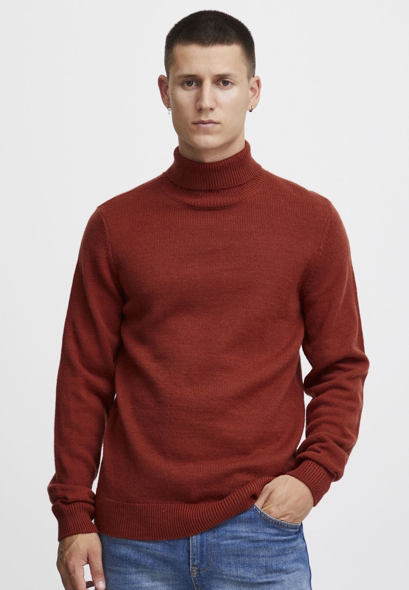 Pulover turtleneck roșu ruginit fabricat dintr-o țesătură moale. Are manșete și tiv cu nervuri, cu o siluetă ajustată. Purtați-l cu blugi albaștri.