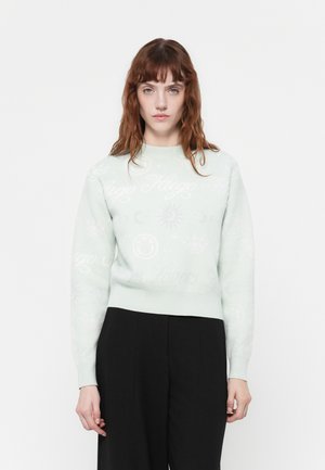Mintgroene trui met een ronde hals, versierd met lichte symbolen en tekst. Zachte textuur, nauwsluitend in de taille, gecombineerd met zwarte broeken.