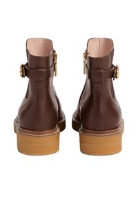 Para brązowych skórzanych botków za kostkę z złotymi klamrami i detalami zamka błyskawicznego, jasnobeżowe wyściełane podeszwami, widziane z tyłu.