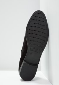 Suola in suede nero con fondo in gomma testurizzata. Presenta una punta affilata e il logo del marchio sul tallone. Taglia 40 indicata sulla suola.