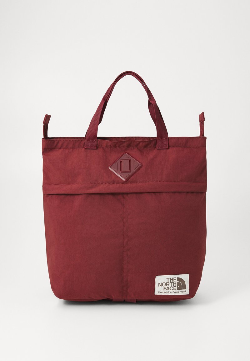 Bordowa torba typu tote z podwójnymi uchwytami, naszywką w kształcie diamentu u góry oraz białą metką z logo "The North Face" w prawym dolnym rogu.