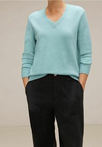 Helles türkisfarbenes V-Ausschnitt-Pullover aus weichem Strick, mit gerippten Bündchen und Saum. Kombiniert mit schwarzen Hosen, die eine legere Passform zeigen.