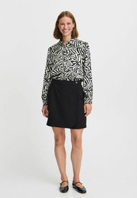 Gonna nera con un design avvolgente asimmetrico, abbinata a una camicia a maniche lunghe con un motivo geometrico in bianco e nero.