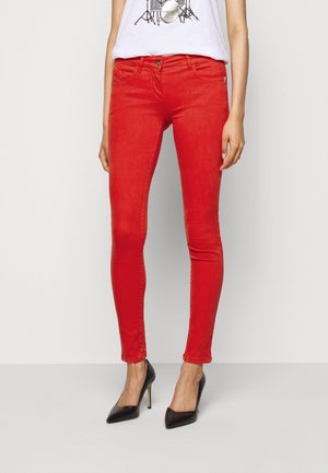 Jean skinny rouge en denim, au design ajusté, avec des poches avant et une fermeture à bouton. Portés avec des talons aiguilles noirs.