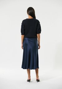Dunkelblauer Strickpullover mit kurzen Puffärmeln, kombiniert mit einem seidigen, fließenden dunkelblauen Midirock. Sanfte Textur, eleganter Fall und minimalistisches Design.