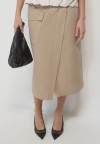 Jupe midi beige avec une poche latérale, au design épuré et à la texture subtile. Assortie à des escarpins noirs à bout pointu et à une pochette noire.
