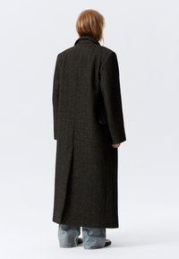 Lang mørk brun uldfrakke med en struktureret design, en krave med hak og en lige pasform. Har en enkelt slidse bagpå og sidelommer.