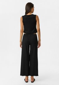Zwarte textuur crop top gecombineerd met brede zwarte broek, met een eenvoudig ontwerp en geen zichtbare patronen of hardware accenten.