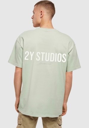 Világos zöld, oversized pamut póló, amelyen a hátsó részen nagy fehér felirat olvasható: "2Y STUDIOS". Kerek nyakkivágással és rövid ujjakkal készült.