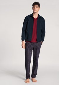 Heren loungewear set met een marineblauwe ritsjack, een rode V-hals top en gestreepte pyjamabroeken in tinten blauw, rood en wit.