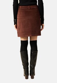 Ruskea corduroy-minihame, jossa on vartalonmyötäinen muotoilu, takataskut ja vyötärönauha. Yhdistettynä mustiin polvipitkiin saappaisiin ja teksturoituihin sukkiin.