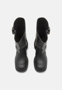 Botas de cuero negro con punta redondeada, acabado suave, altura hasta la mitad de la pantorrilla, hebilla decorativa en el lado y forro interior suave.