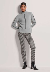 Hellgrauer Rollkragenpullover mit schwarzen Streifen, kombiniert mit schwarz-weißen gemusterten, tapered Hosen und schwarzen, hochhackigen Stiefeletten.