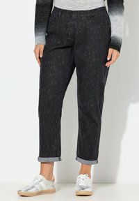 Černé džíny z denimu s jemnými reliéfními vzory, ohrnutými lemy a volnějším střihem, doplněné stříbrnými a béžovými teniskami.
