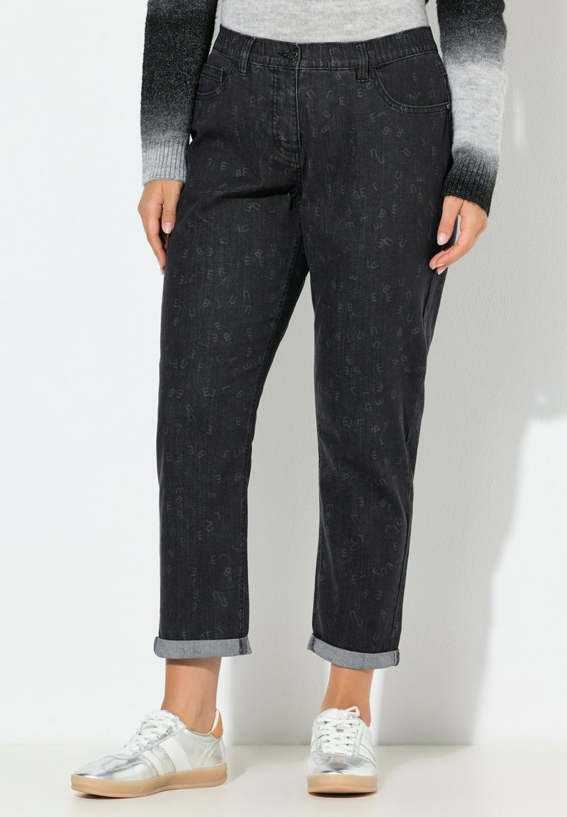 Černé džíny z denimu s jemnými reliéfními vzory, ohrnutými lemy a volnějším střihem, doplněné stříbrnými a béžovými teniskami.