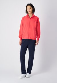 Rode ritsjack gemaakt van zacht materiaal, gecombineerd met marineblauwe, rechte broek en witte sneakers. Eenvoudig ontwerp zonder patronen.