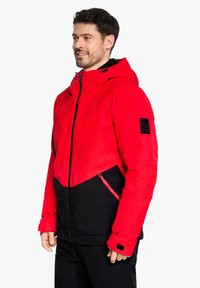 Rot und schwarz isolierte Jacke mit Kapuze, durchgehendem Reißverschluss und Taschen, mit strukturiertem Finish und schwarzen Akzentdetails an den Ärmeln.