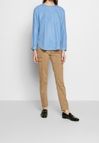 Jasnoniebieska koszula z długim rękawem, okrągłym dekoltem i kieszenią na piersi, zestawiona z khaki spodniami z kieszeniami po bokach oraz czarnymi mokasynami.