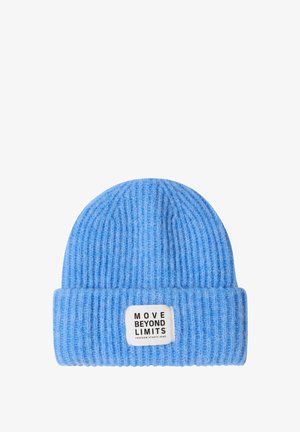 Bonnet bleu clair en maille côtelée avec revers, arborant une étiquette blanche rectangulaire avec le texte noir "MOVE BEYOND LIMITS". Texture douce.