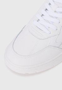 White sneaker featuring a smooth leather upper, rounded toe, textured accents, and white laces, with stitching details visible on the surface.