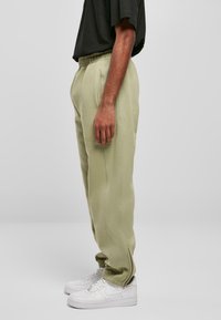 Light green sweatpants with an elastic waistband, side pockets, and ankle cuffs, paired with white sneakers. Smooth texture, casual fit.
