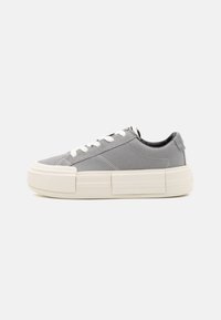 Graue Low-Top-Sneaker mit weißen Schnürsenkeln und dicker, cremefarbener Gummisohle, seitliche Ansicht auf hellem, schlichtem grauem Hintergrund.
