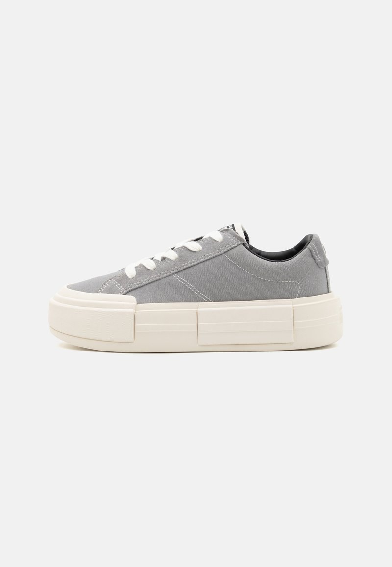 Graue Low-Top-Sneaker mit weißen Schnürsenkeln und dicker, cremefarbener Gummisohle, seitliche Ansicht auf hellem, schlichtem grauem Hintergrund.
