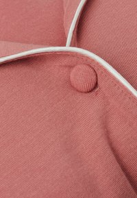 Růžová texturovaná tkanina s malým kulatým knoflíkem a bílým lemováním podél okraje. Materiál vypadá jemně a tkaně.
