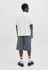 Hvid bomulds T-shirt med korte ærmer, parret med grå knæ-lange shorts. Sorte sko og hvide sokker med sorte striber fuldender looket.