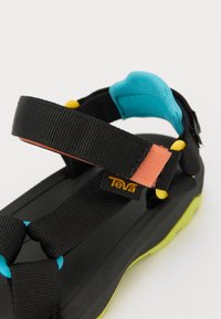 Svart sandal med justerbare remmer i svart, blått, oransje og gult. Har en teksturert svart såle og en fremtredende logo-merke.