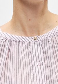 Gros plan sur le cou et le haut de la poitrine d'une personne portant un chemisier rayé rose clair avec un bouton décoratif près du col.