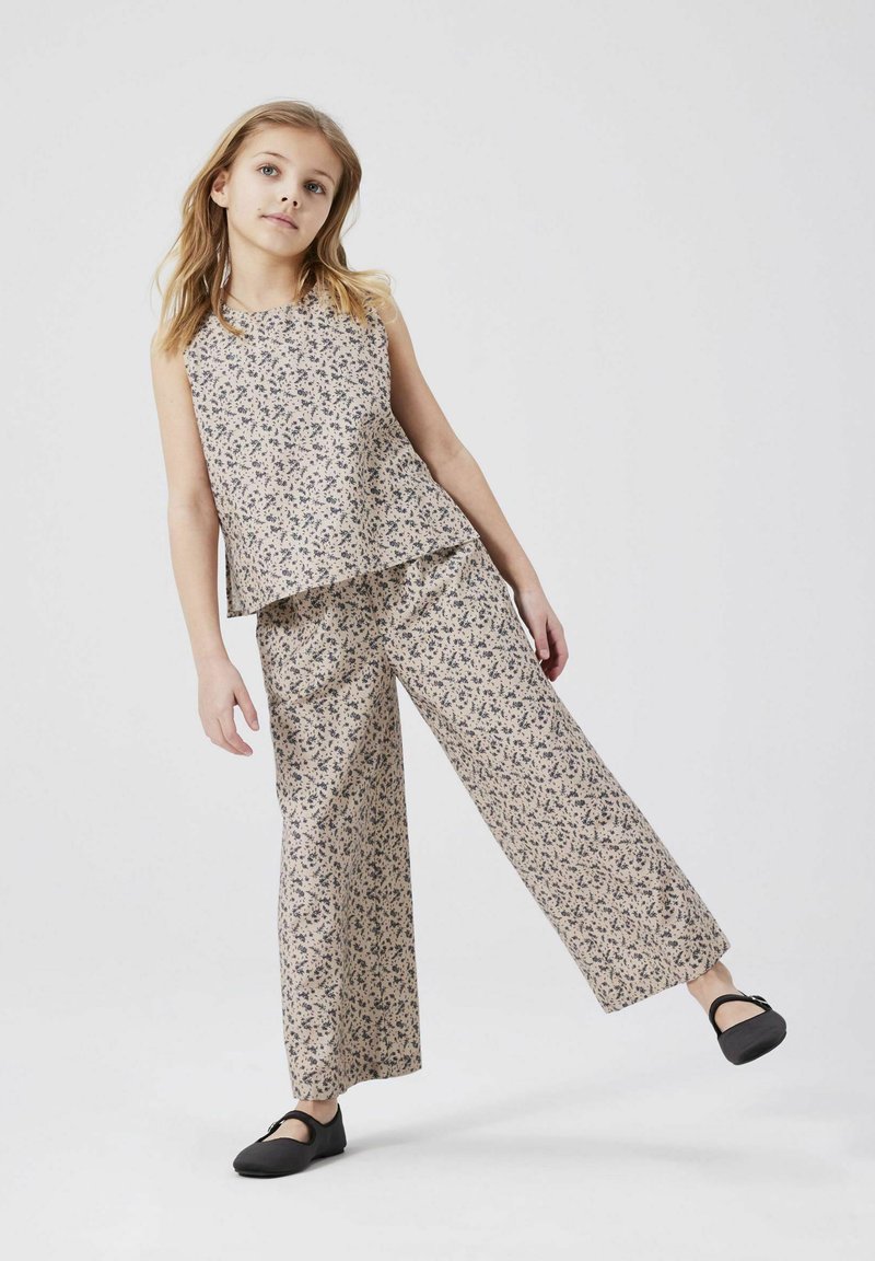 Lätt, ärmlös blommig topp och vida byxor i beige med blå mönster. Svarta skor fulländar outfiten. Slät textur.