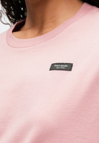 Ροζ βαμβακερό t-shirt με στρογγυλή λαιμόκοψη. Διαθέτει μια μαύρη ετικέτα υφάσματος με λευκό κείμενο που αναγράφει "kate spade NEW YORK." Λείο υλικό.