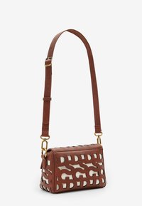 Brązowa torebka na ramię z wyciętymi, przeplatającymi się literami na białym tle oraz regulowanym paskiem ze złotą klamrą.