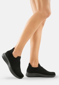 Schwarze Strick-Slipper mit strukturiertem Obermaterial, freiliegendem Knöchel-Design und flexibler schwarzer Gummisohle.