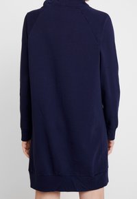 Granatowa sukienka dresowa z długimi rękawami, ściągaczami na mankietach i zaokrąglonym dołem, wykonana z miękkiego materiału o gładkiej fakturze.