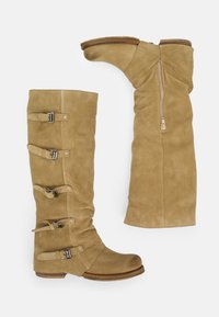 Botas altas de ante color canela, una en posición vertical con cinco correas con hebilla, la otra de lado mostrando una cremallera lateral y un tacón bajo de madera.