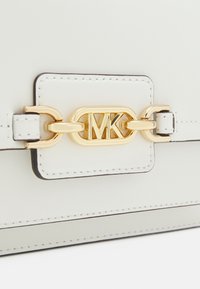 Hvid lædertaske med guldfarvet kæde og sammenflettet "MK" logo detalje på klappen.