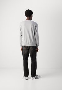 Sudadera gris de Manga Larga con puños y dobladillo acanalados, combinada con jeans oscuros y zapatillas deportivas grises, vista desde la parte de atrás.
