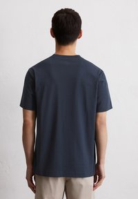 Marineblaues T-Shirt mit kurzen Ärmeln, aus weicher Baumwolle, mit Rundhalsausschnitt und lockerer Passform, von hinten vor einem schlichten Hintergrund gezeigt.