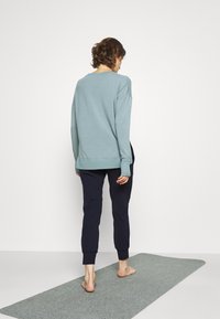 Hellblaues Sweatshirt mit rundem Ausschnitt, langen Ärmeln und Seitenschlitzen, kombiniert mit dunkelblauen Jogginghosen mit Rippbündchen, auf einer grauen Matte.