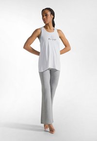 Valkoinen toppi, jossa on "Re-pose" -teksti, ja harmaat joogahousut. Sileä kangas, rento istuvuus ja hieman kaartuva helma yläosassa sekä lahkeet levenevällä leikkauksella.